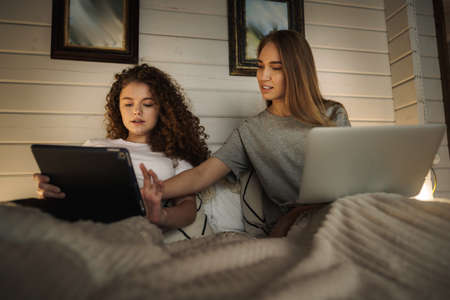 Two beautiful women lying in bed, holding a laptop