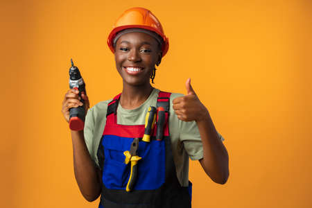 Smiling young african american woman in hardhat holding screwdriver tool in studioの写真素材