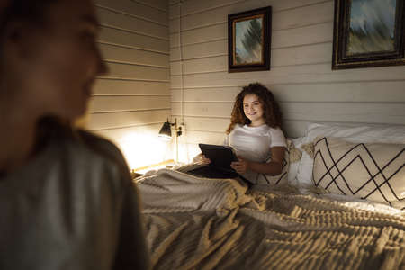 Teenage girl laying on bed using a laptop with mom sitting on bedの写真素材