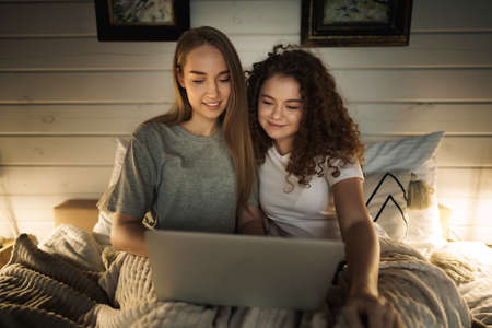 Two beautiful women lying in bed and watching movies on laptopの写真素材