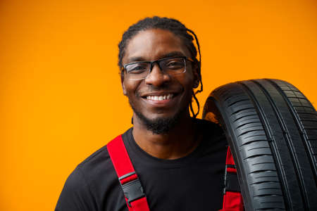 African american car service worker with car tyre against yellow backgroundの写真素材
