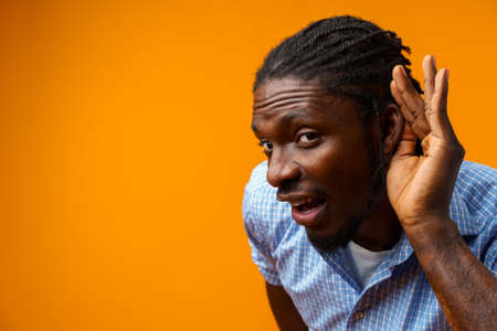 Portrait of attentive man in casual shirt putting hand to ear to hear betterの写真素材