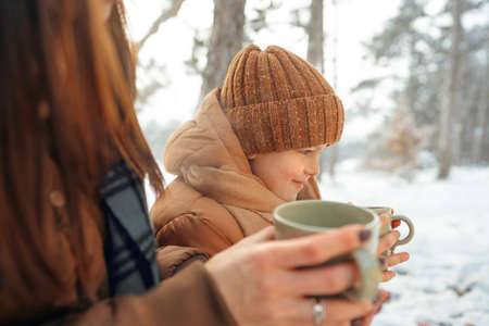 Young woman with a son in winter forest on a picnic drink hot teaの写真素材