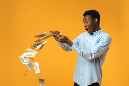 Excited black guy holding stack of Dollars in yellow studioの写真素材