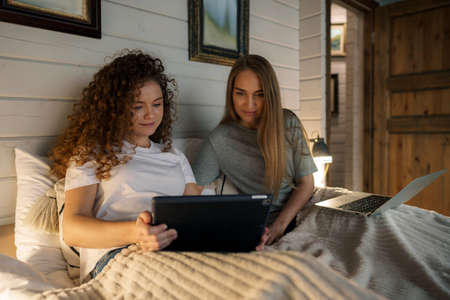 Two beautiful women lying in bed, holding a laptopの写真素材