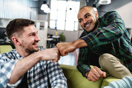 Two handsome men sitting together in the office and giving each other a fist bumpの写真素材