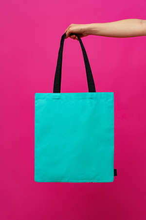 Female hand holding eco or reusable shopping bag against pink backgroundの写真素材