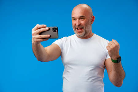 Happy middle-aged man with a phone in his hands against blue background