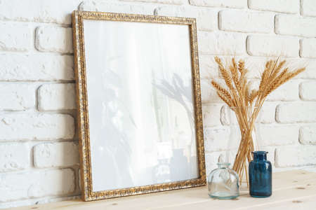Vase with ears of wheat and photo frames against brick wall