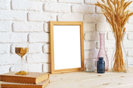 Vase with ears of wheat and photo frames against brick wall