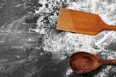 Pile of flour in wooden spoon on dark background