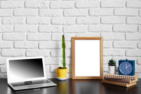 Worktable with laptop, stationery and decorations in home office with blank photo frame