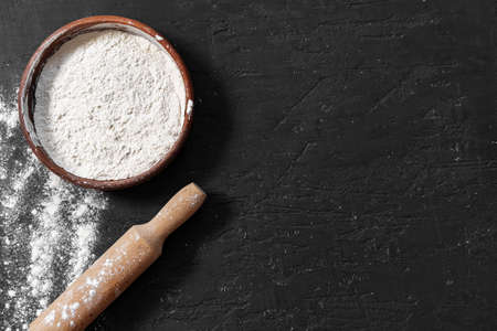Scattered flour with rolling pin on black background