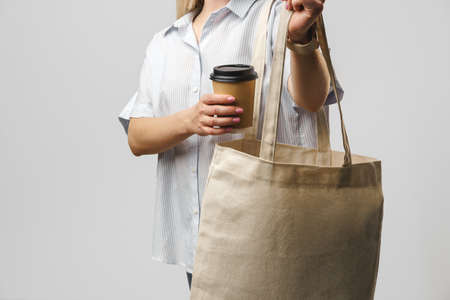 Cropped woman with cotton bag and paper coffee cup, studio shotの写真素材