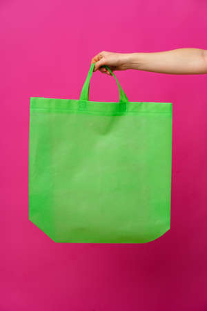 Female hand holding eco or reusable shopping bag against pink backgroundの写真素材