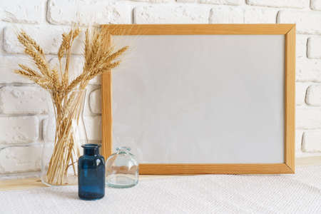 Vase with ears of wheat and photo frames against brick wall
