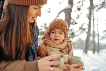 Young woman with a son in winter forest on a picnic drink hot teaの写真素材