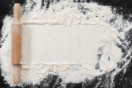 Scattered flour with rolling pin on black backgroundの写真素材