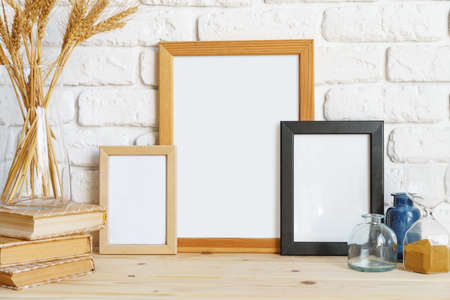 Vase with ears of wheat and photo frames against brick wall