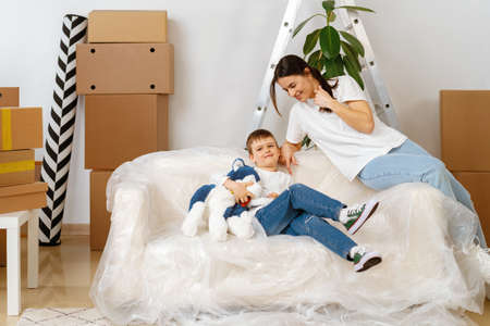 Beautiful smiling woman and little boy with cardboard boxes moving to new home