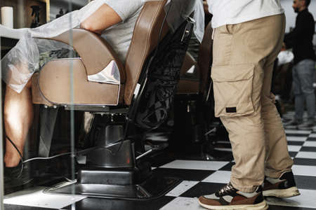 Barber guy gives a haircut to a bearded man sitting in a chair in a barbershopの写真素材