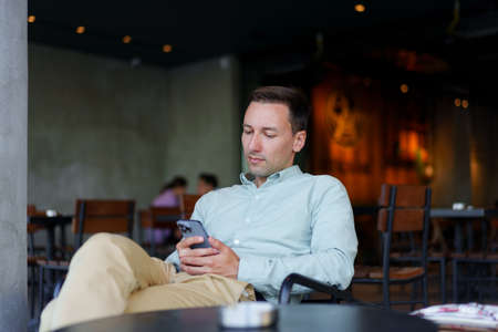 Confident businessman using smartphone sitting in restaurant