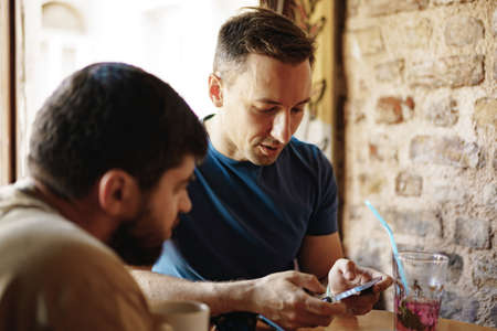 Two adult male friends sitting and talking in cafe.