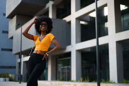 Photo of a stylish young black woman with curly hair wearing orange crop top walking in the street