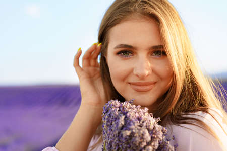 Young woman in dress holding bouquet of flowers standing in lavender fieldの写真素材