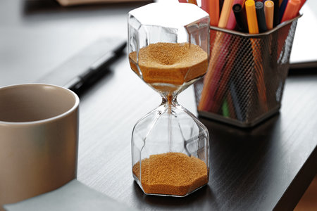 Hourglass with golden sand pouring inside on wooden background