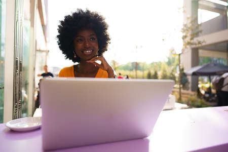Happy beautiful young black woman using laptop in cafeの写真素材