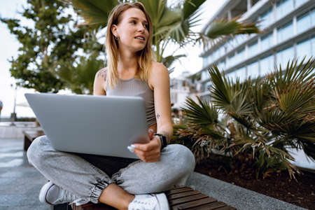 Young beautiful casual woman working on a laptop sitting on the bench in the streetの写真素材