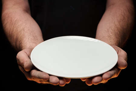 Male hands holding empty plate on dark background, lack of food, hunger concept.の写真素材