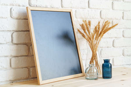 Vase with ears of wheat and photo frames against brick wall
