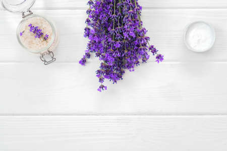 Herbal oil and lavender flowers on white wooden background