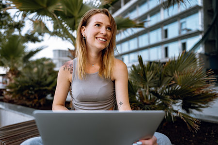 Young beautiful casual woman working on a laptop sitting on the bench in the streetの写真素材