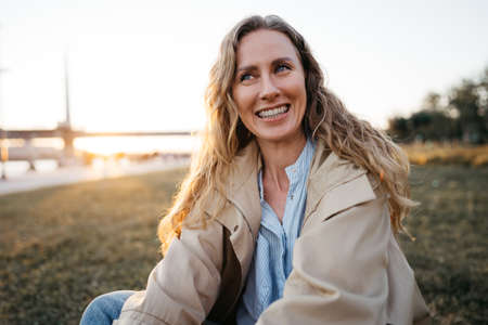 Happy young woman sitting on lawn outdoors in the cityの写真素材