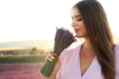 Young woman in dress holding bouquet of flowers standing in lavender fieldの写真素材