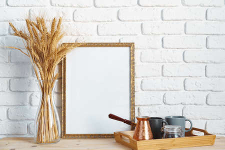 Vase with ears of wheat and photo frames against brick wall