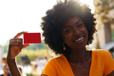 Portrait of young american woman with afro hairstyle holding red plastic credit cardの写真素材