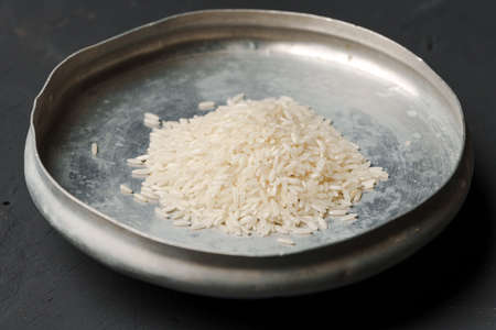 Heap of dry rice in a bowl on black background, lack of food, hunger conceptの写真素材
