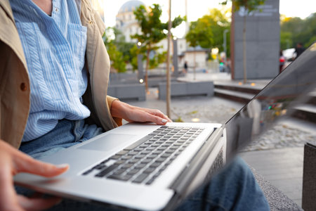 Close up of female hands typing on computer keyboard of a laptop sitting in the streetの写真素材