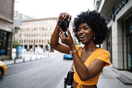 Smiling African american woman using professional camera at a streetの写真素材