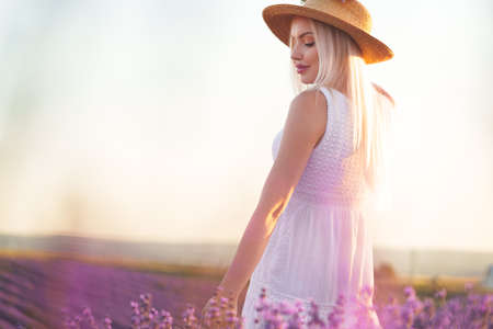 Young woman in long white dress standing in lavender fieldの写真素材
