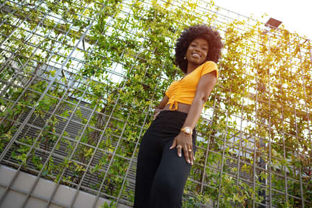 Portrait of a beautiful young african american woman posing against backdrop of green hedgeの写真素材