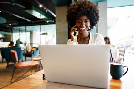 Young woman having phone conversation using laptop at cafeteriaの写真素材