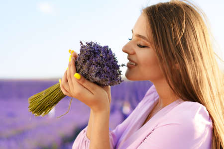 Young woman in dress holding bouquet of flowers standing in lavender fieldの写真素材