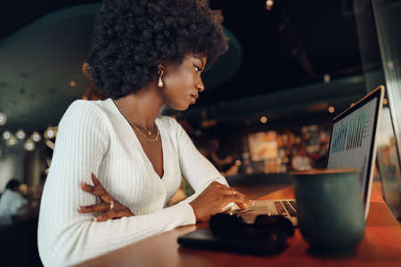 Smiling young african woman sitting with laptop in coffee shopの写真素材