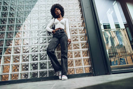 African young woman looking happy while posing against glass wallの写真素材