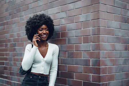 Portrait of happy african young woman talking on cellphone in cityの写真素材